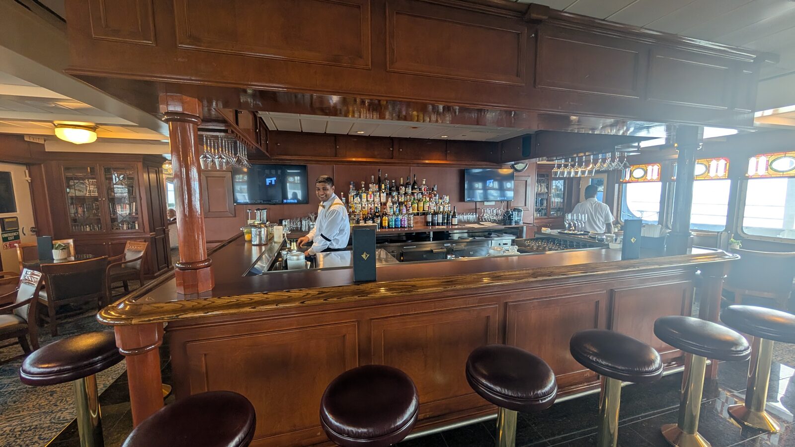 The wood-paneled bar on Victory II with leather bar stools and a bartender