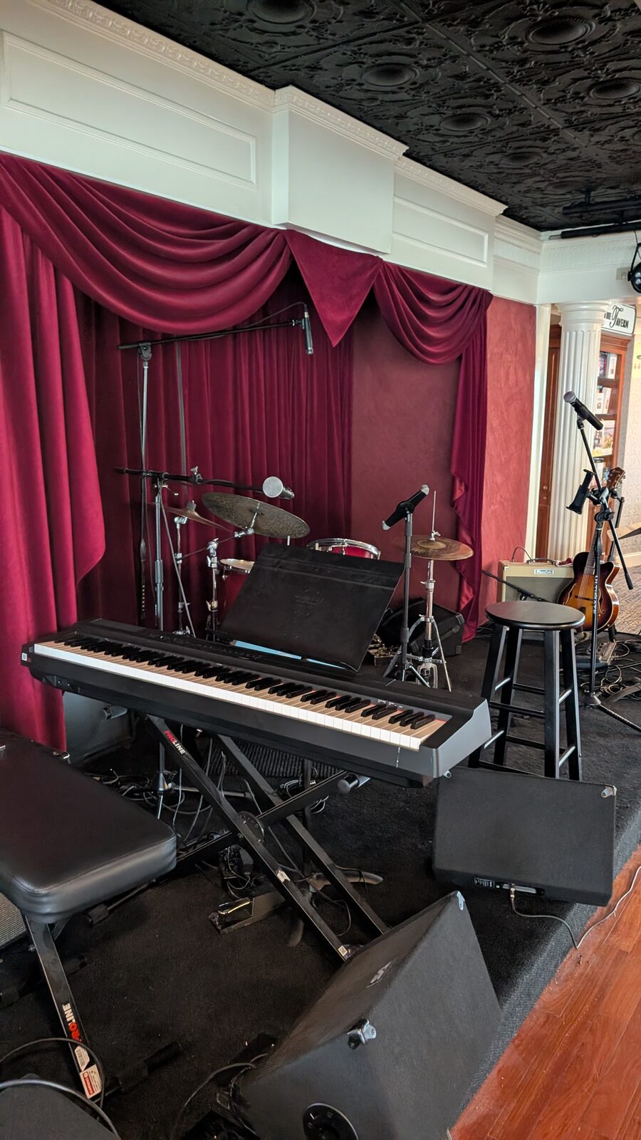 Small stage with red curtains, keyboard, and drum kit in the Victory II lounge