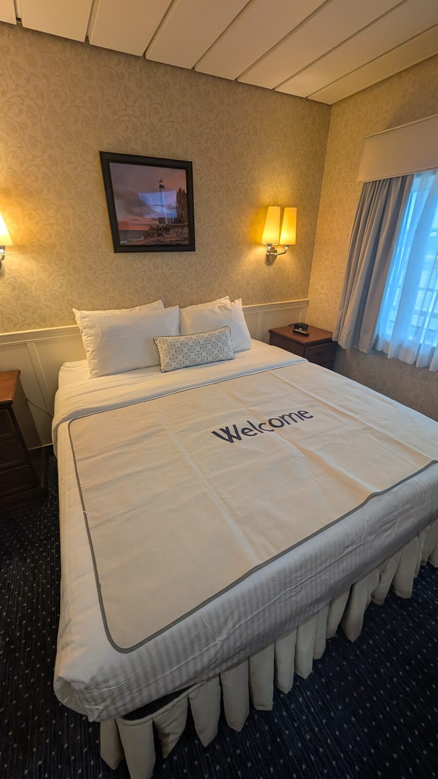 Victory II stateroom with a queen bed, bedside lamps, and a framed lighthouse print