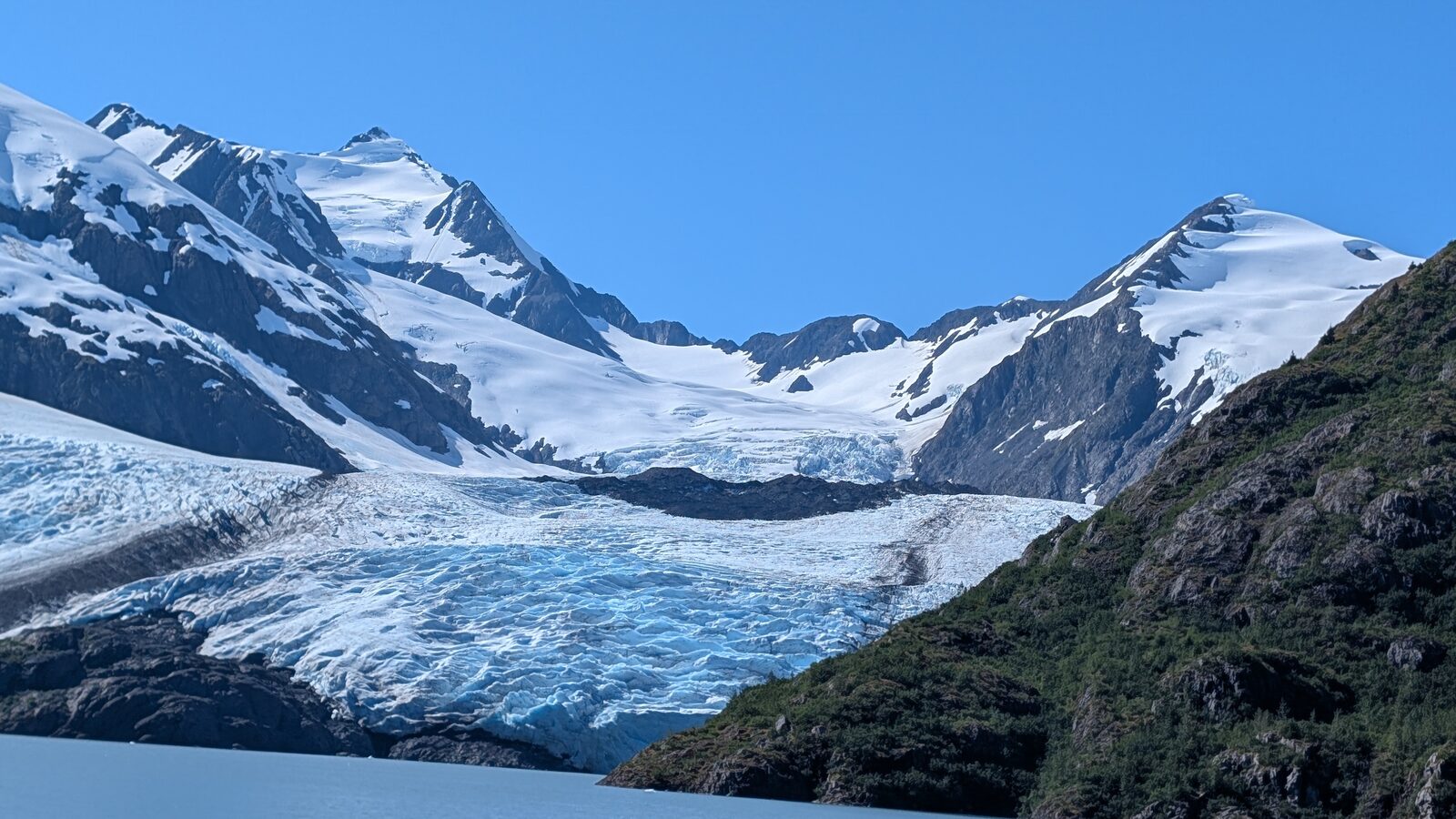 Portage Glacier flowing down between snow-covered peaks to the edge of Portage Lake