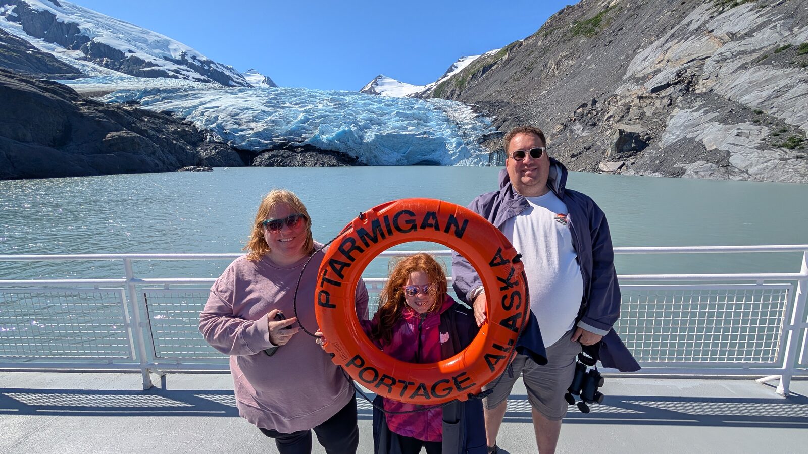 Andrew Hooker and family on the deck of the Portage Glacier boat, holding a Ptarmigan life ring with the glacier behind them