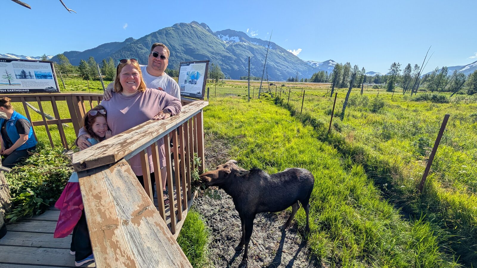 Andrew Hooker and family at a boardwalk railing watching a moose graze at the Alaska Wildlife Conservation Center